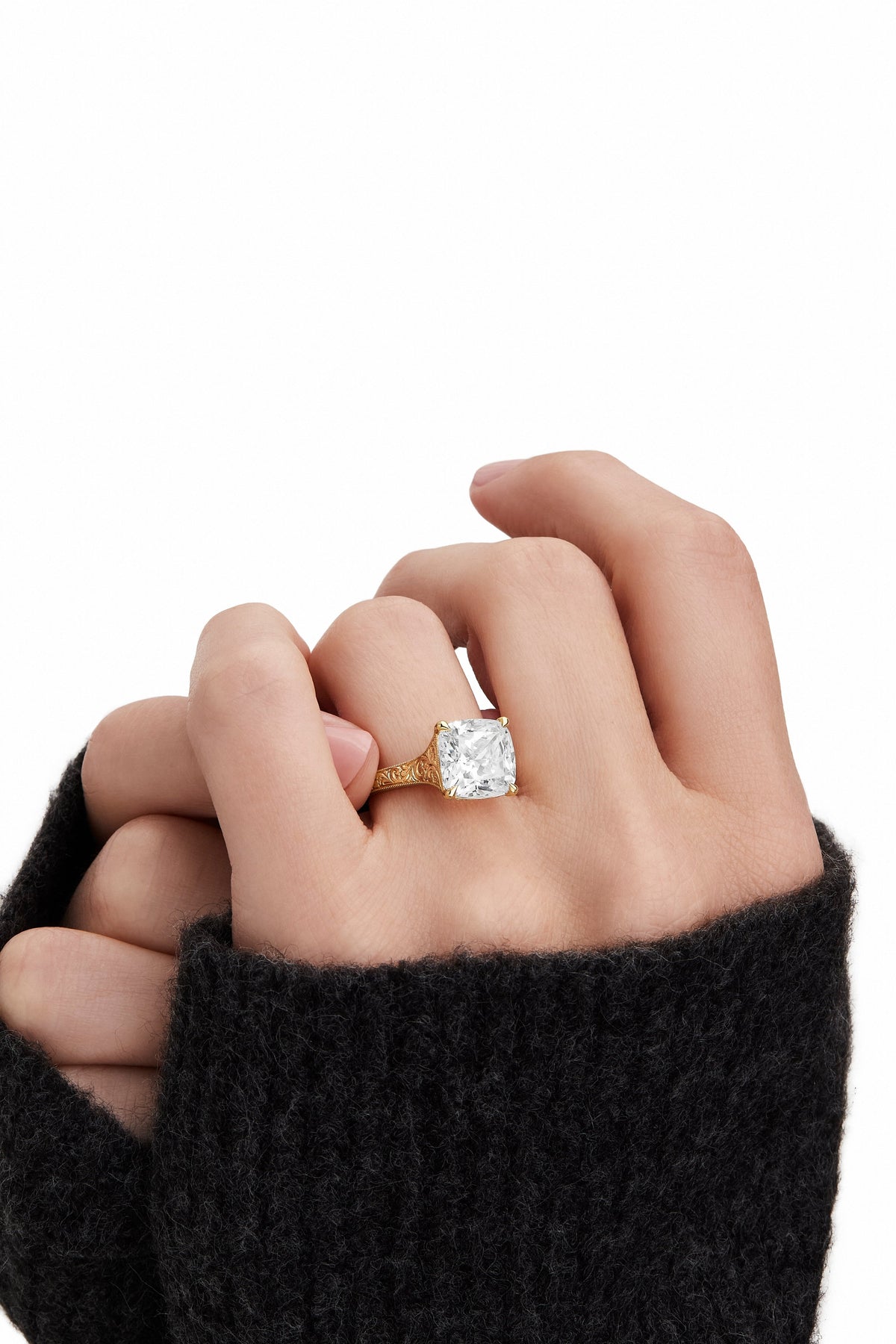A cushion-cut diamond ring set on a gold band with intricate engraving, worn on a finger.