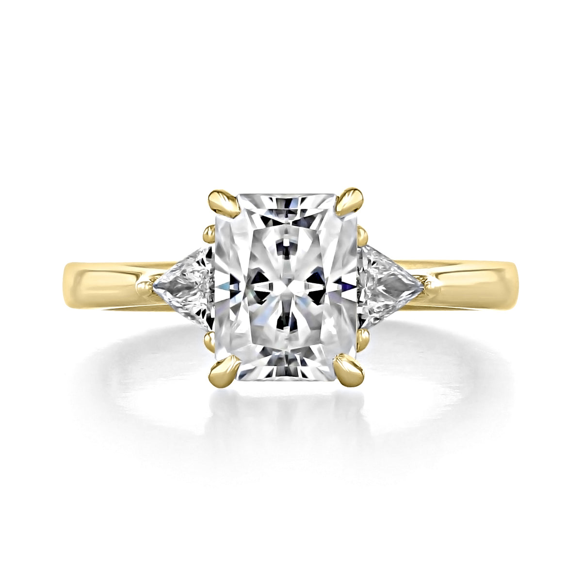 The Emery | Trillion Three-Stone Engagement Ring is a 14k yellow gold ring featuring a large radiant cut center stone flanked by two triangular side stones.