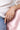 A close-up lifestyle shot of a person's hand resting on a pink satin surface, wearing a silver band ring with a pink pear-shaped diamond and a thin silver spacer ring.