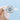 An Isla | Round Halo Solitaire Engagement Ring by evertrue by Icing On The Ring, featuring a round center diamond in a square-shaped halo on a plain 14k white gold band, held between two fingers.