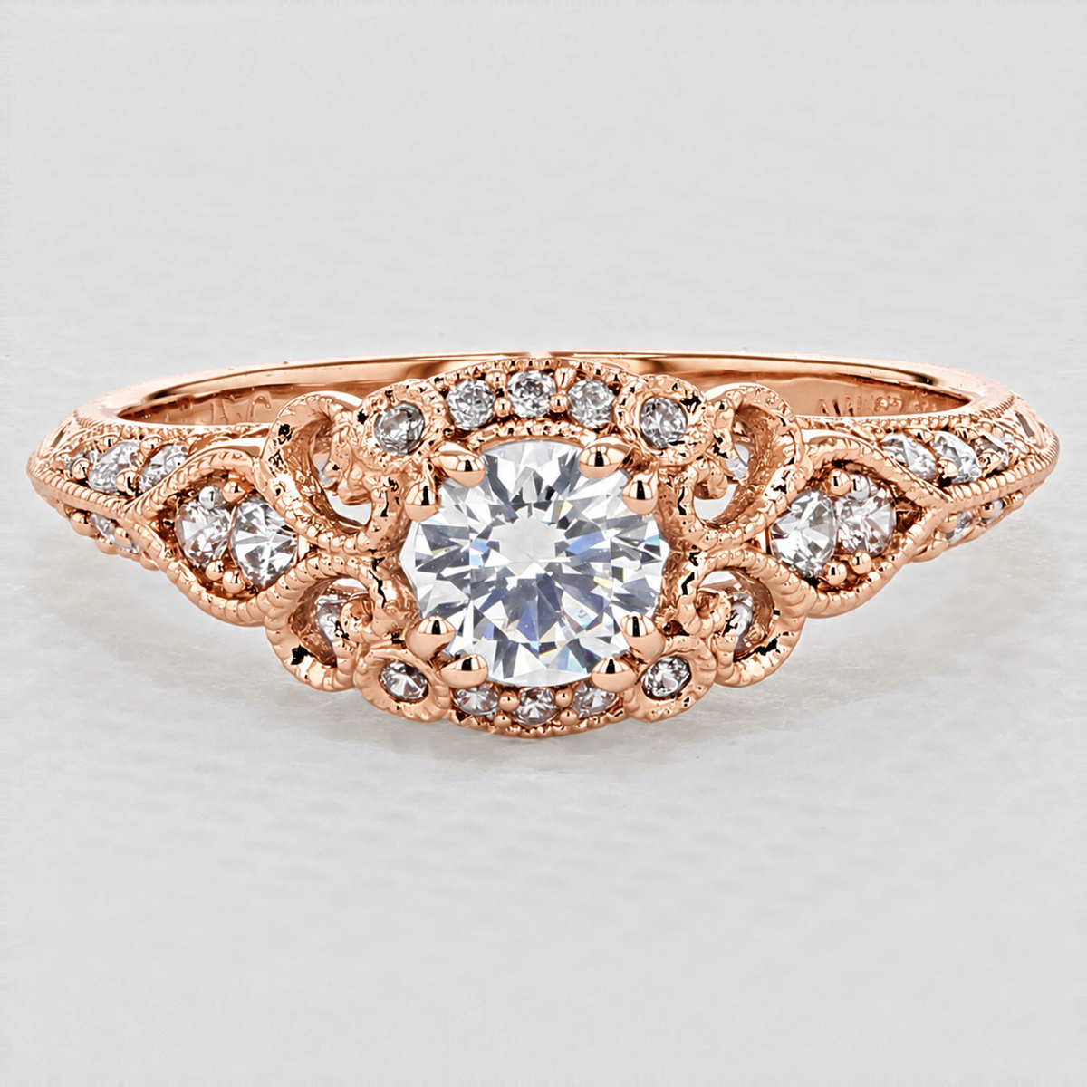 Abel | Halo Engagement Ring by Gabriel & Co. in rose gold, featuring a round center diamond surrounded by ornate, filigree-style metalwork and smaller accent diamonds along the band.