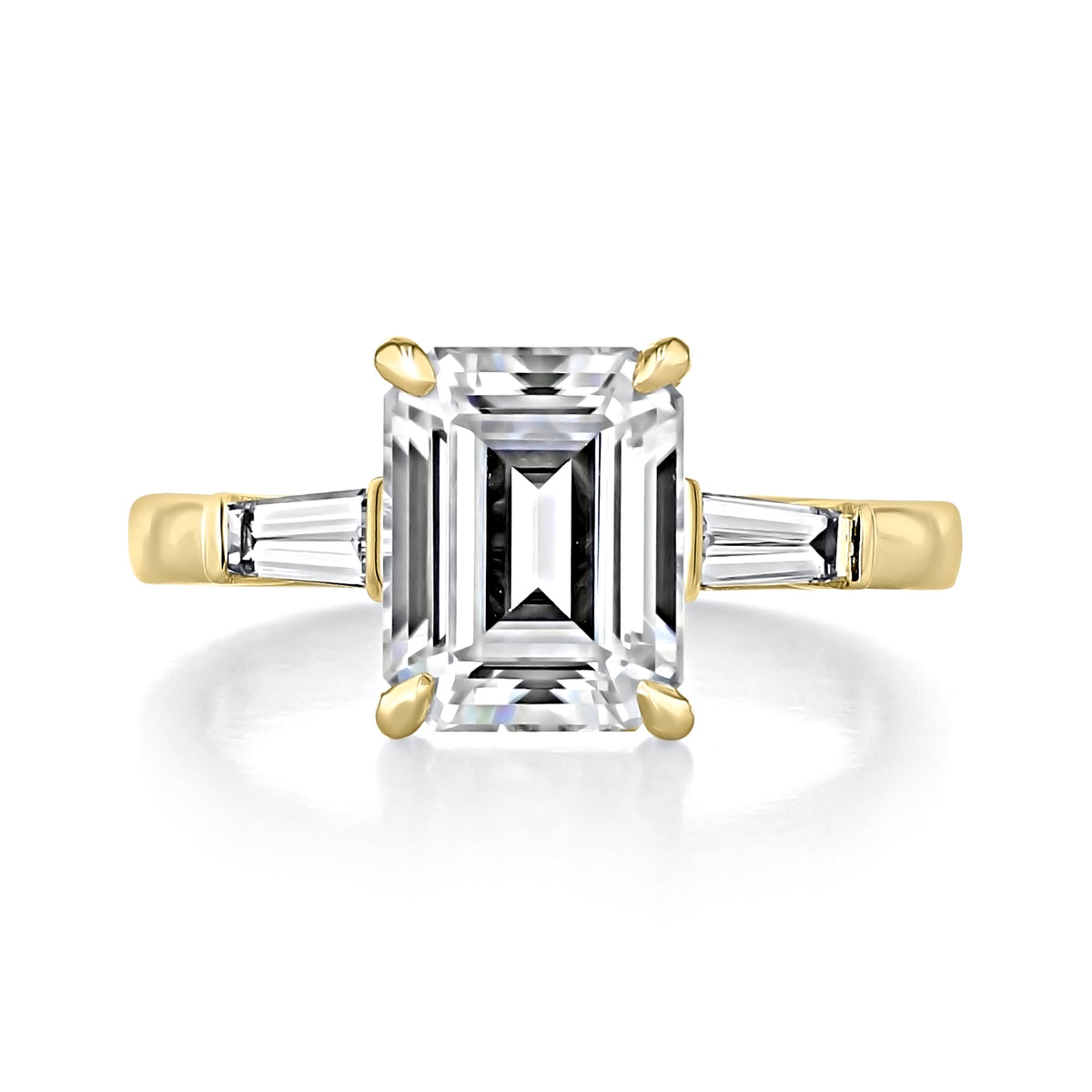 Vivienne | Emerald Three-Stone Engagement Ring by Icing On The Ring featuring a 14k yellow gold band, a large emerald-cut center diamond, and two tapered baguette-cut side stones.
