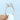 A hand with white nail polish holds a Vivienne | Emerald Three-Stone Engagement Ring, featuring a large emerald cut center stone flanked by two tapered baguette stones.