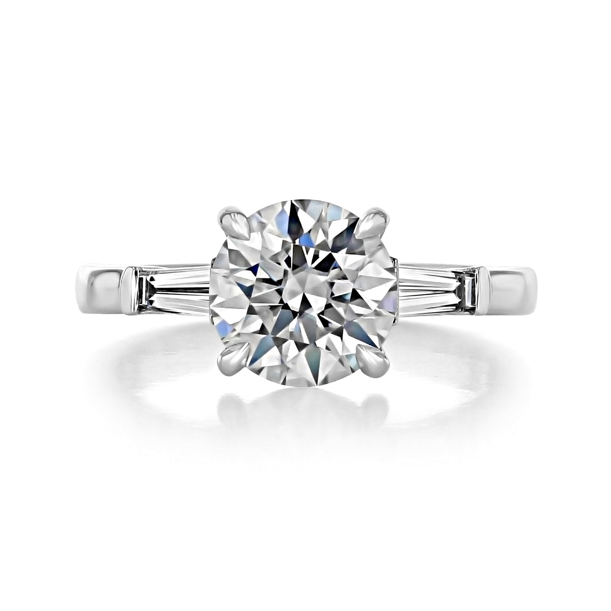 Vivienne | Round Three-Stone Engagement Ring featuring a round brilliant-cut diamond with a tapered diamond baguette on each side, set in a 14k platinum band.