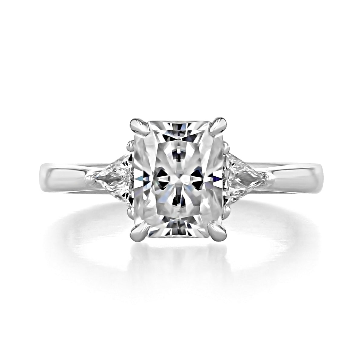 An Emery | Trillion Three-Stone Engagement Ring featuring a large rectangular Radiant Cut Moissanite center stone flanked by two smaller trillion-cut diamonds on a silver-toned band.